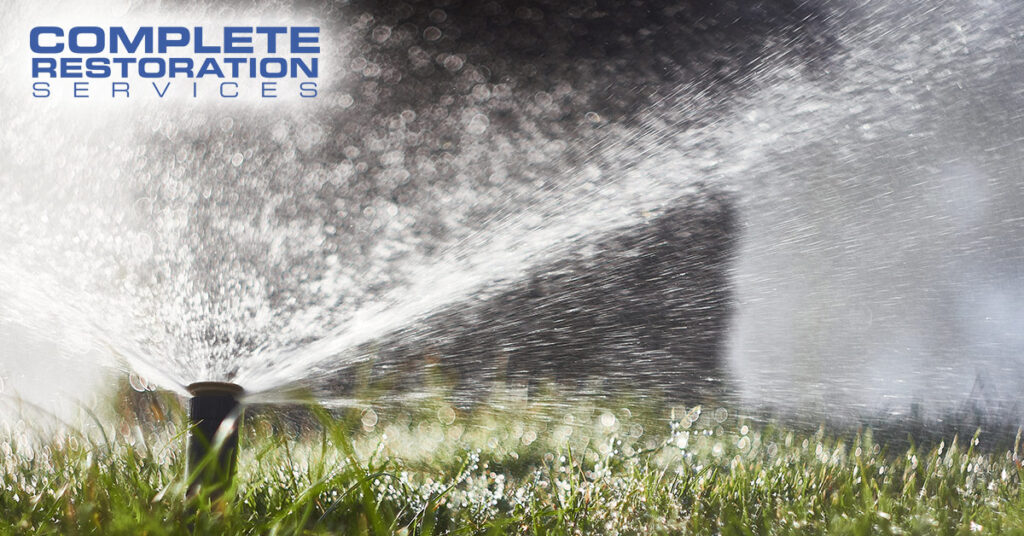 Lawn sprinkler spraying water over grass with "Complete Restoration Services" text in the corner.