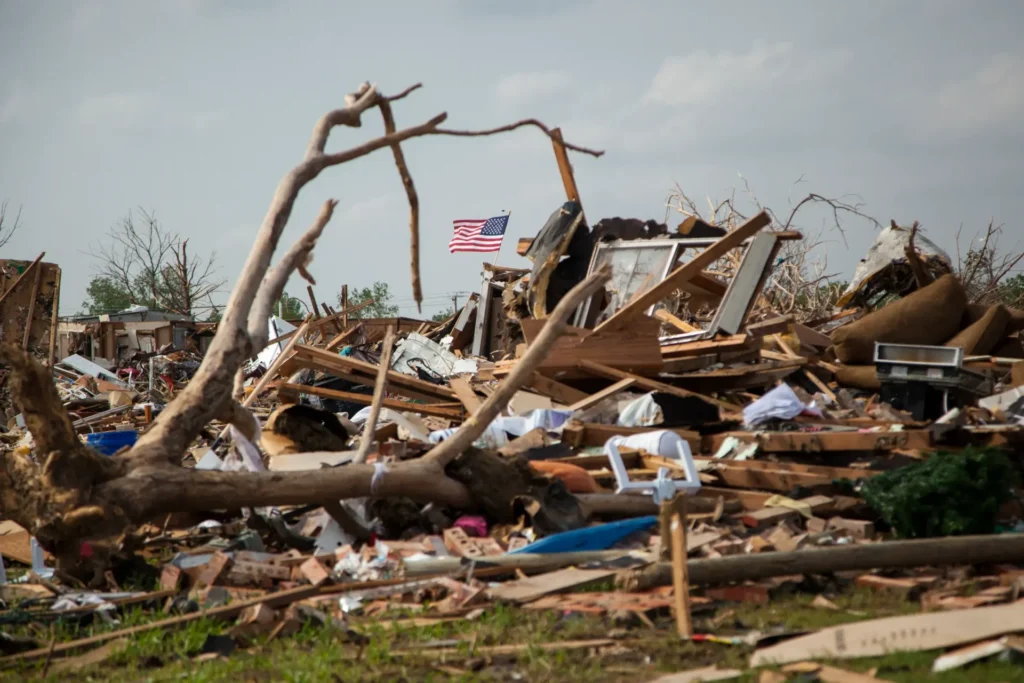 Debris and fallen trees from destruction with an American flag waving in the background.