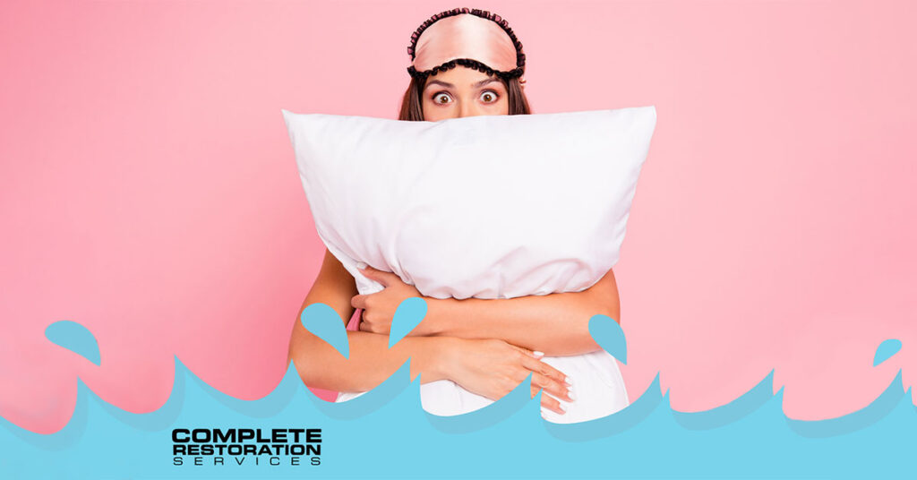 Woman wearing a sleep mask hugging a white pillow against a pink background.