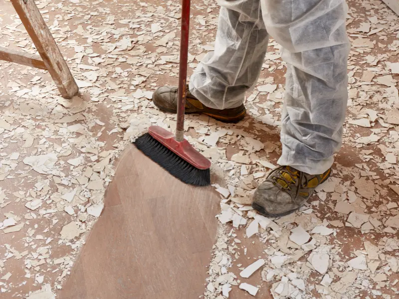 Person sweeping up paint chips or debris from a floor with a broom. construction cleanup services