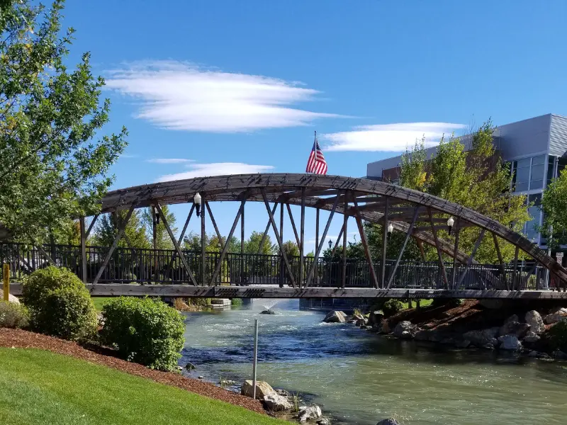 Metal pedestrian bridge over a river with an American flag and trees on a sunny day. water damage restoration in Caldwell