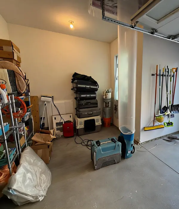 Stacked storage containers, cleaning tools, and boxes in a garage corner with concrete floor. professional restoration company