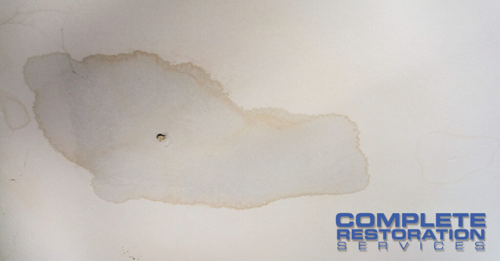 Large water stain with a small hole on a white ceiling.