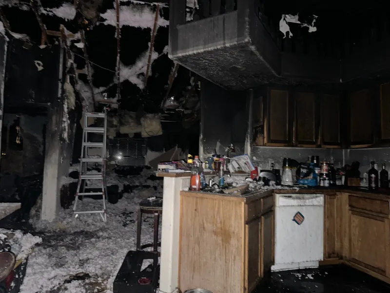 Kitchen severely damaged by fire with soot-covered cabinets, appliances, and debris scattered on the floor. fire damage restoration