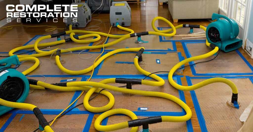 Yellow hoses and blue drying machines set up on a hardwood floor for water damage restoration.