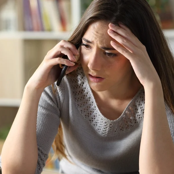 Young woman with long hair looks worried while talking on a phone indoors.